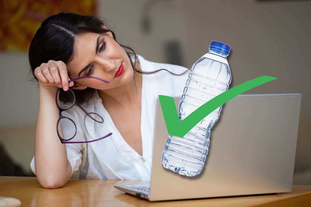 Donna di fronte al computer e bottiglia di acqua