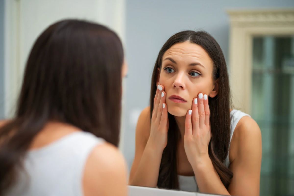 Donna che si guarda allo specchio con le mani sul viso