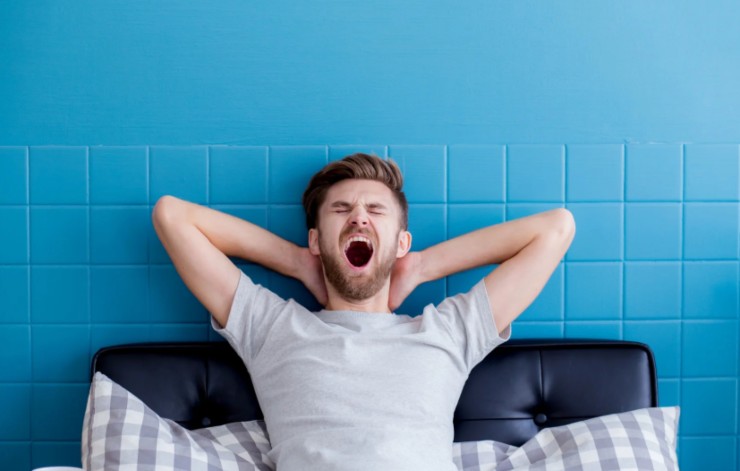 uomo sul divano che sbadiglia con le braccia dietro alla testa