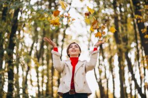 Donna fra gli alberi che lancia foglie per aria